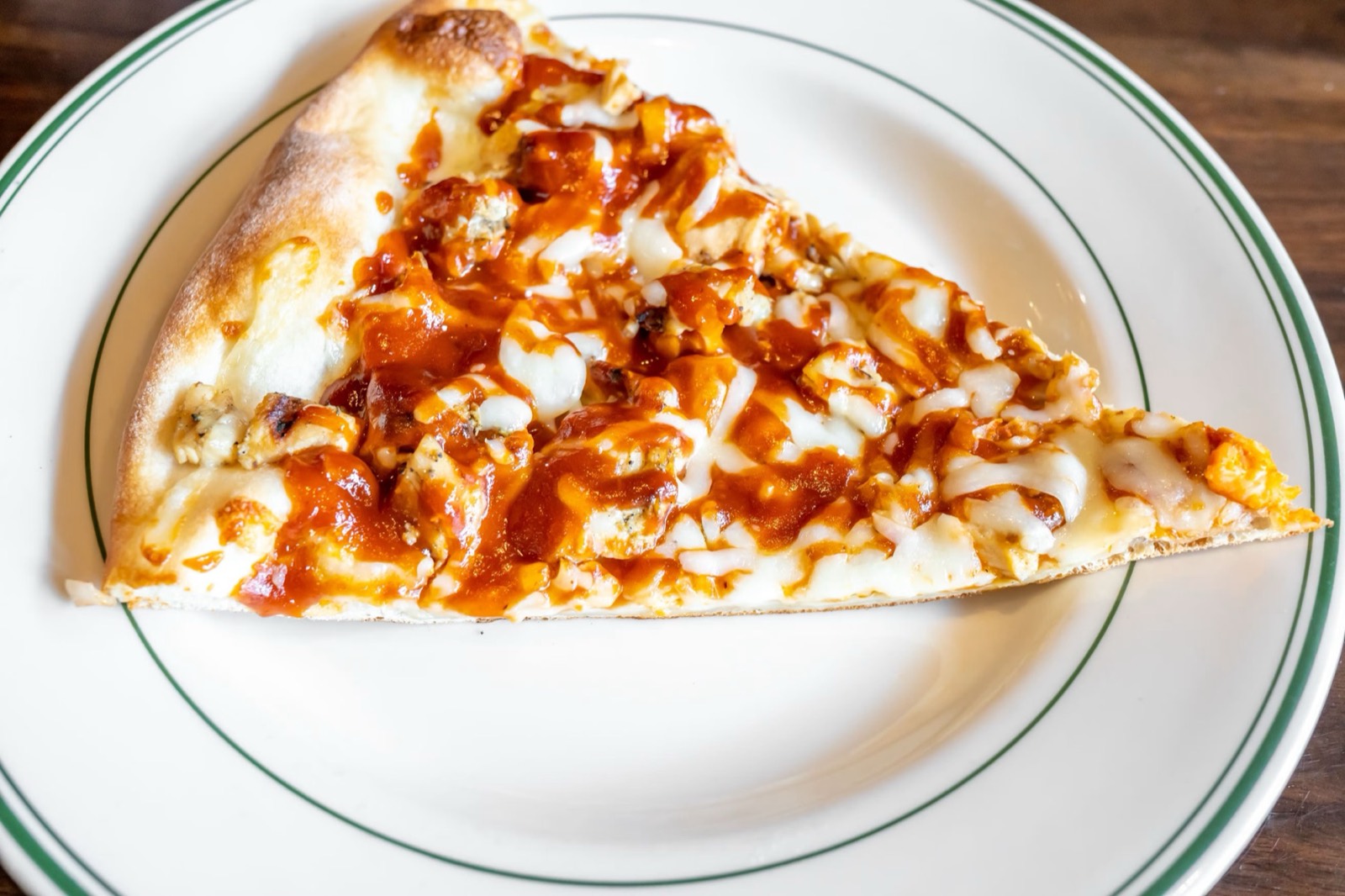 A slice of Nonna Delia's pizza on a green-rimmed plate